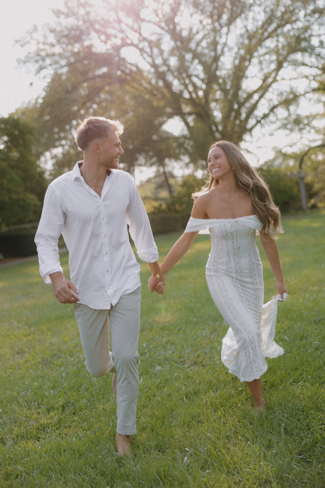 Couple walking hand in hand across an open green field during a golden hour engagement session at Ault Park.