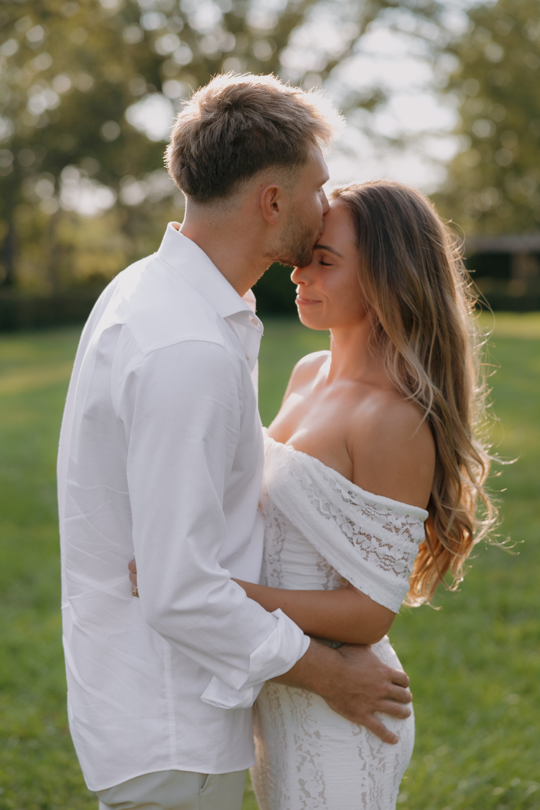 The couple leaning in for a kiss while standing in a grassy field during an engagement session.