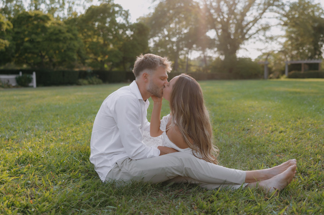 Wide shot of the couple seated together on a hillside overlooking rolling green fields.