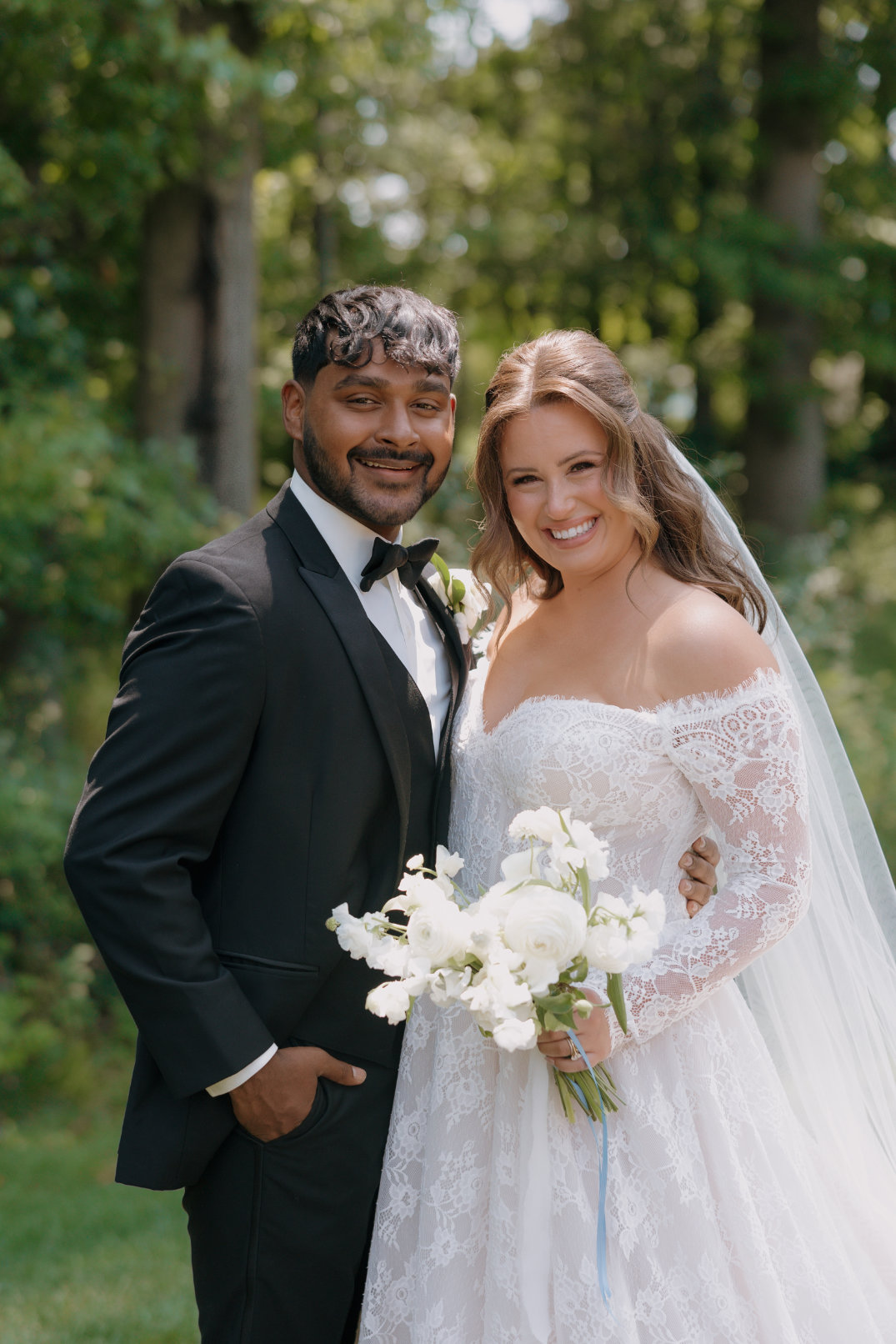 Portrait of the bride and groom smiling together after the ceremony, holding white florals, photographed by Chloe Elizabeth Photography.