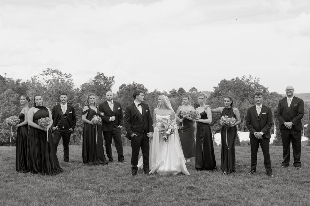 Portrait of the bride and groom standing close together, smiling softly toward the camera in a relaxed outdoor setting.
