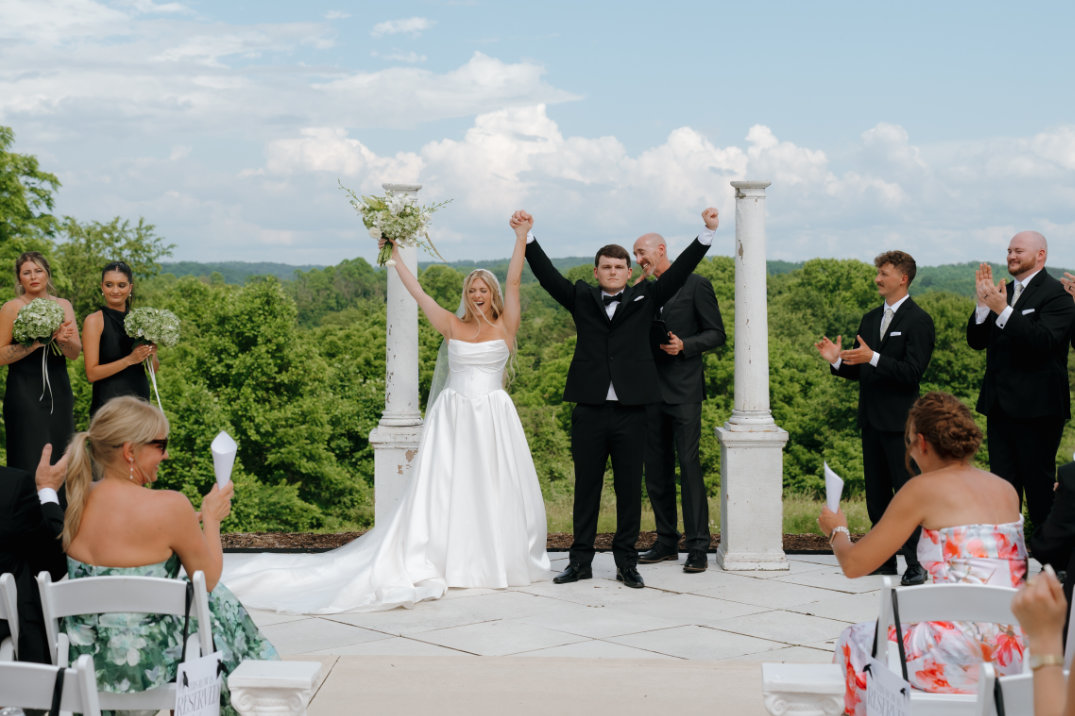 Editorial-style wide ceremony photo with bride and groom celebrating and cheering after exchanging vows.