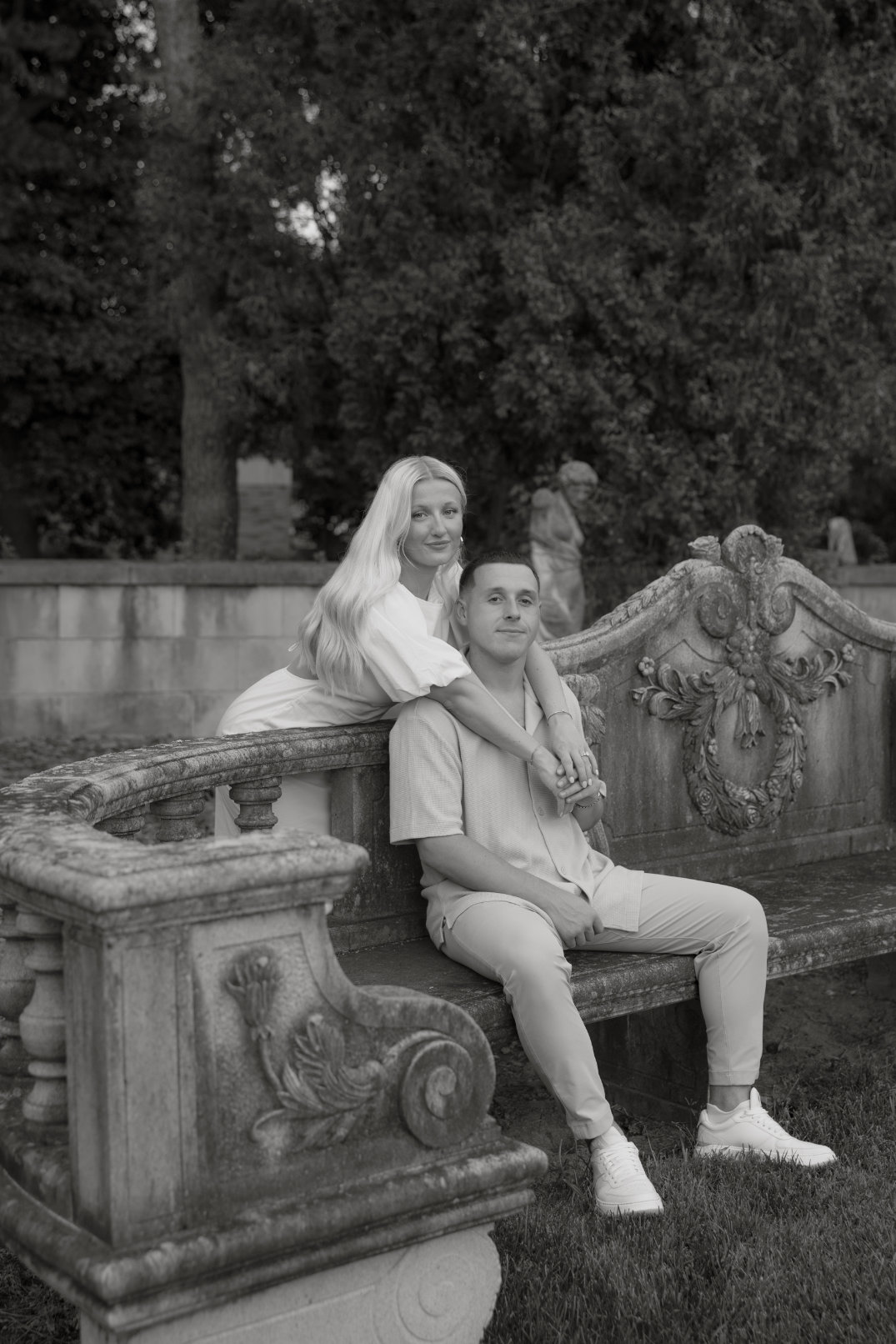 Black and white portrait of the couple seated on a stone bench with sculptural details behind them.