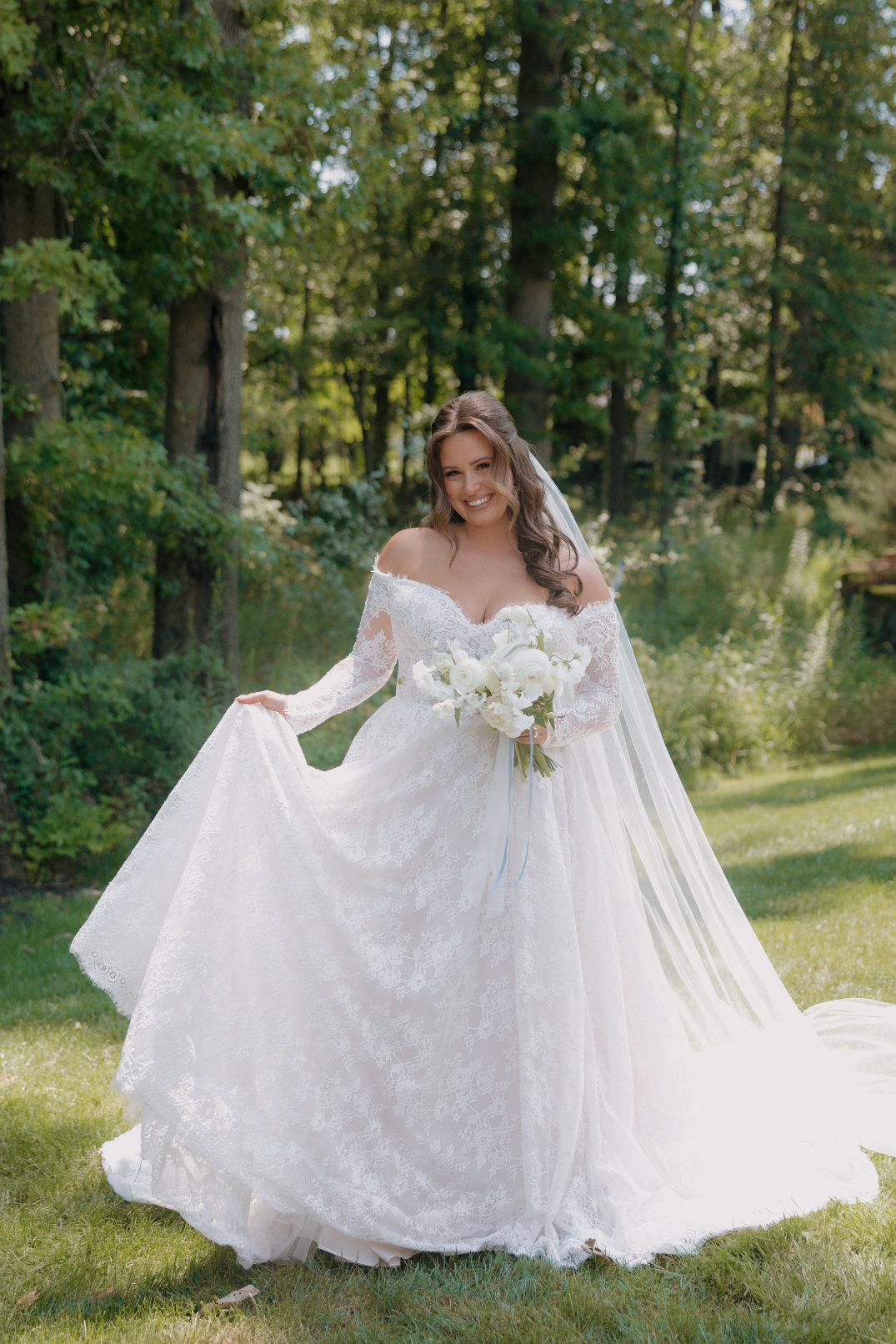Bride holding her bouquet and lifting her dress slightly while standing in the grass.