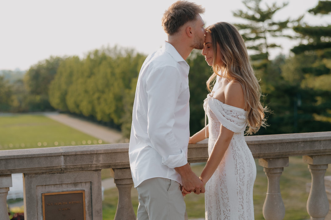 The couple standing together on a stone terrace overlooking a scenic landscape.