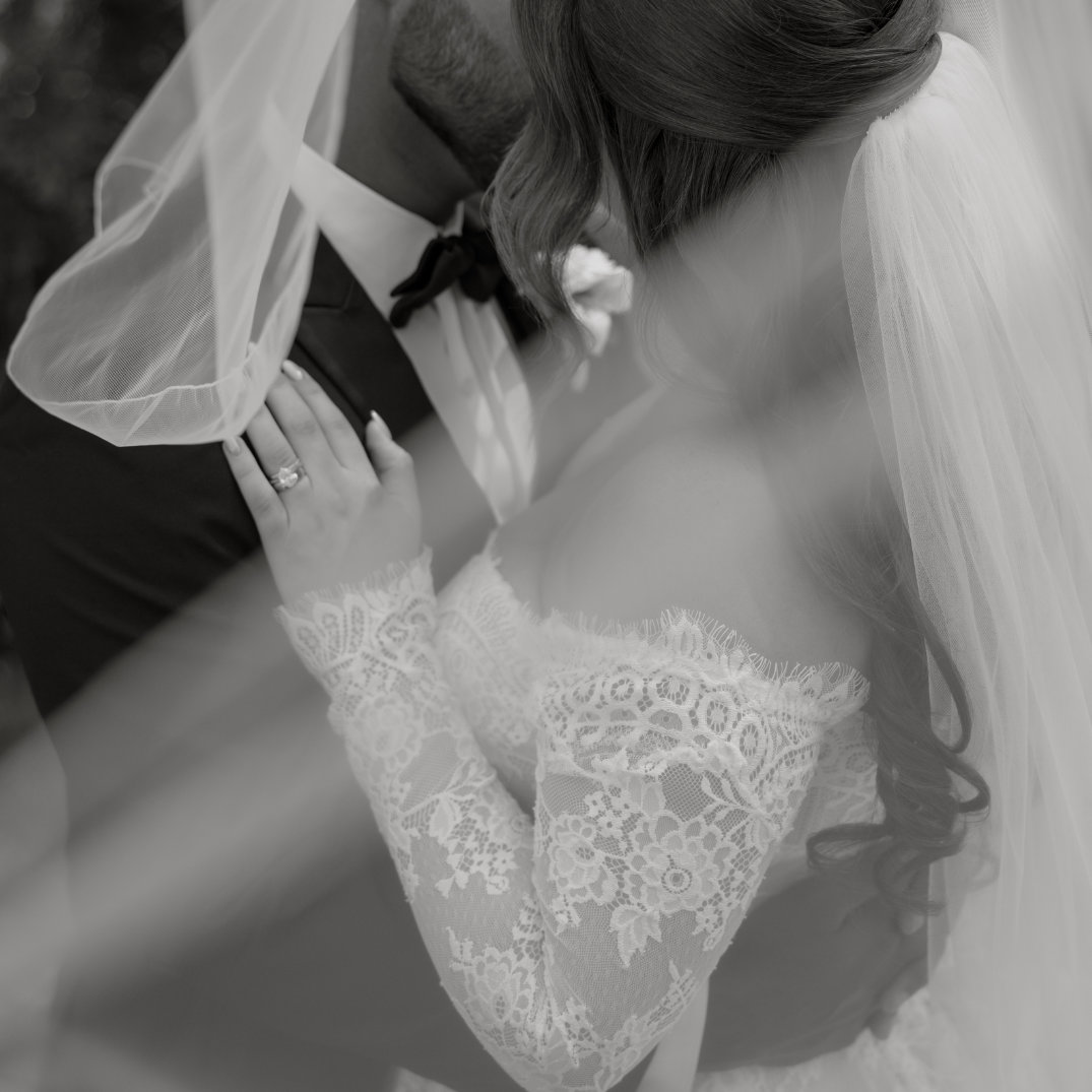 Black and white close-up of the couple embracing beneath the bride’s veil.