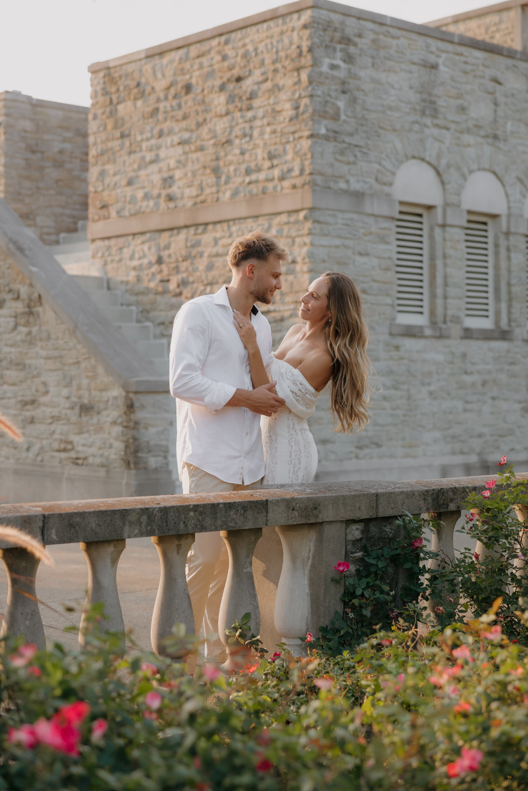 The couple embracing on a stone balcony with ornate railings and historic architecture visible at Ault Park.