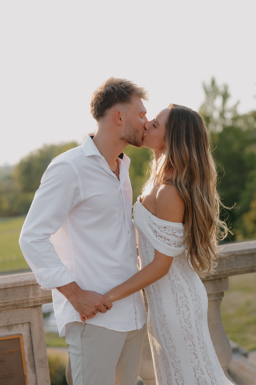 Close-up portrait of the couple standing close together, kissing, near a stone building.
