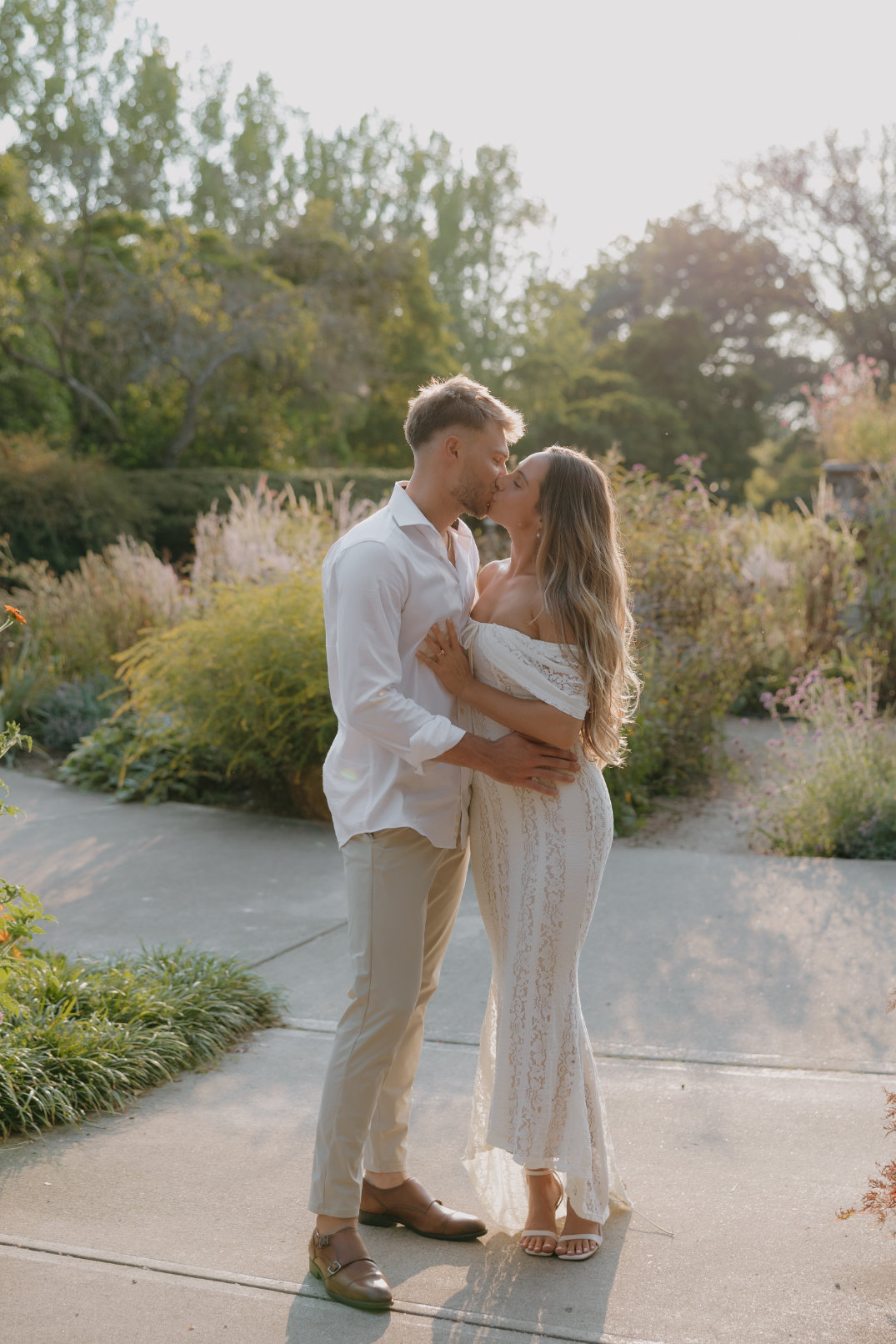 The couple standing together near a pond, embracing with trees and water in the background.