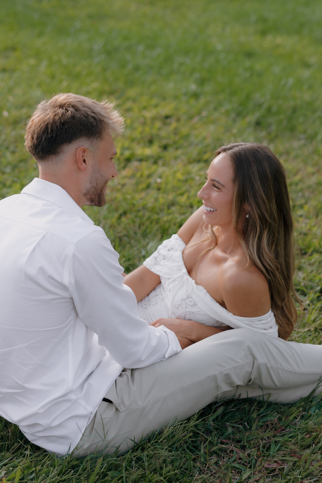 Close-up of the couple embracing, with the woman's in her partner's lap, smiling at each other.