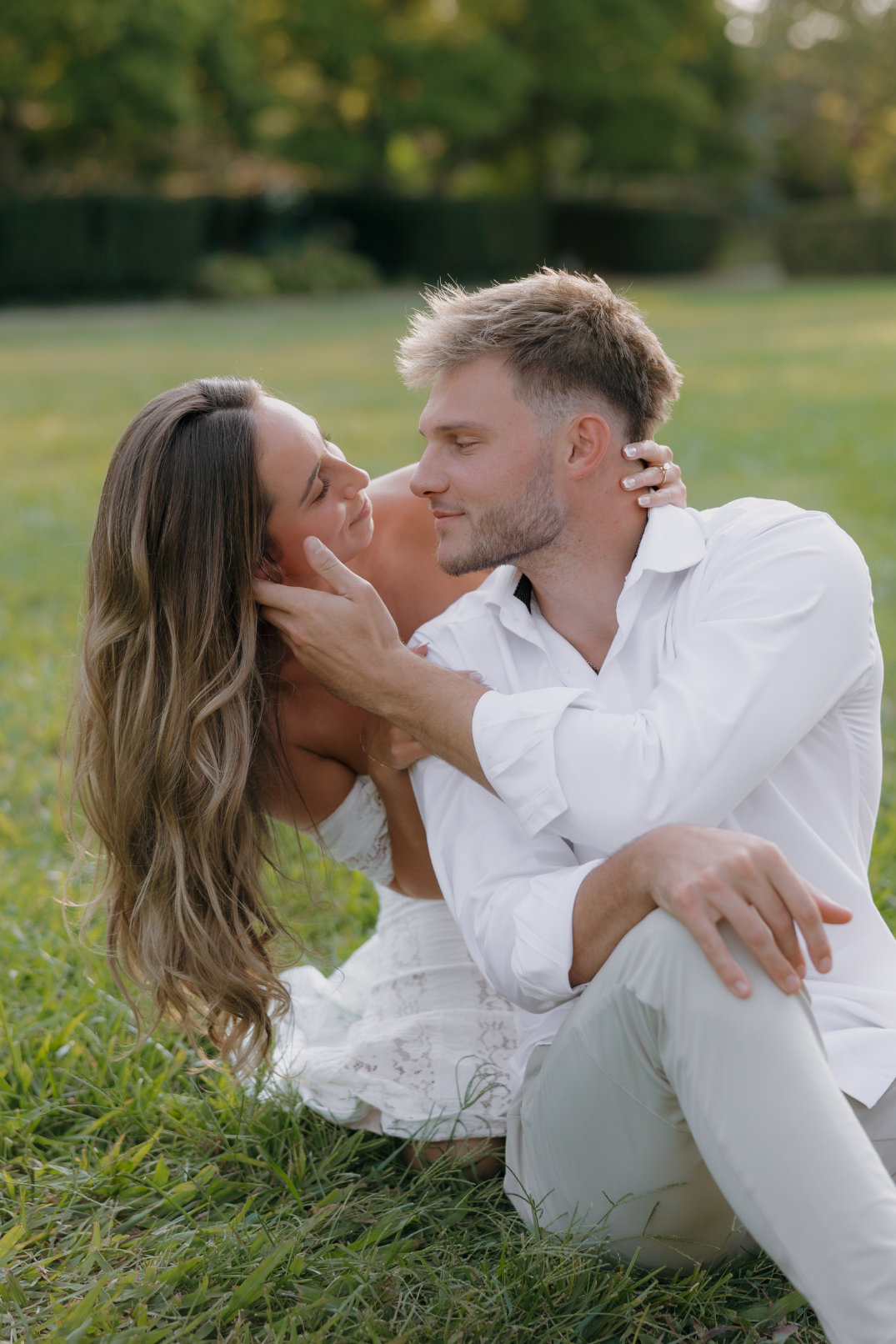 The couple sitting together on the grass, sharing a kiss during their engagement session.