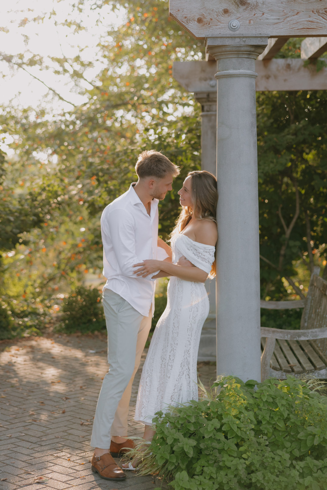 The couple standing together near a white columned pavilion structure during golden hour in Cincinnati, Ohio.