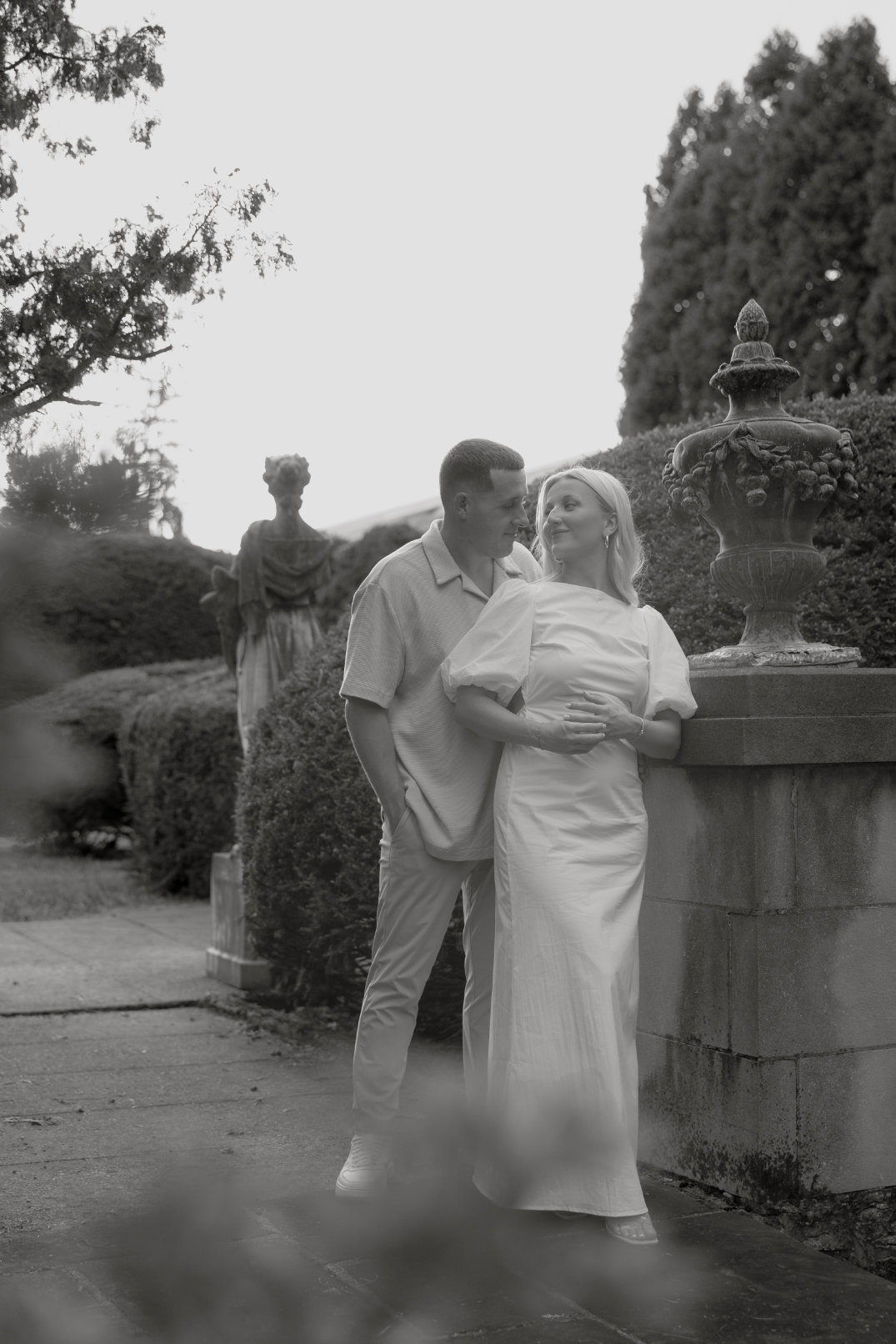 Black and white image of the couple leaning against a stone fountain, sharing a relaxed moment.