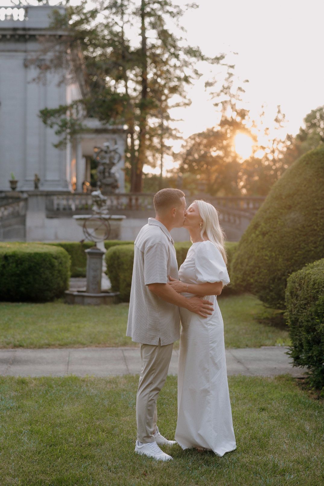 The couple holding one another as sunlight filters through the garden.