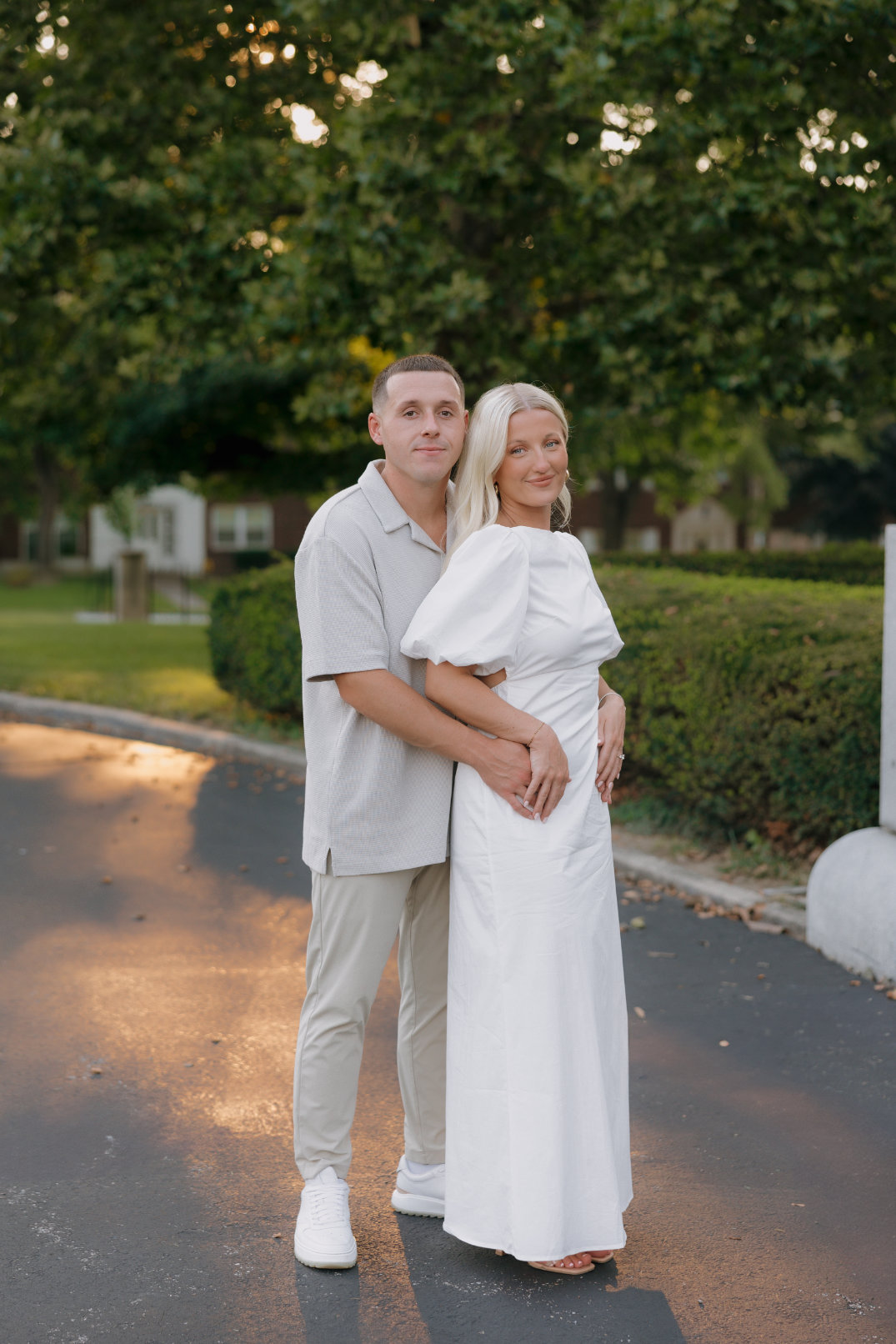 The couple standing together on a paved path with soft evening light behind them, photographed by Cincinnati, Ohio engagement photographer.