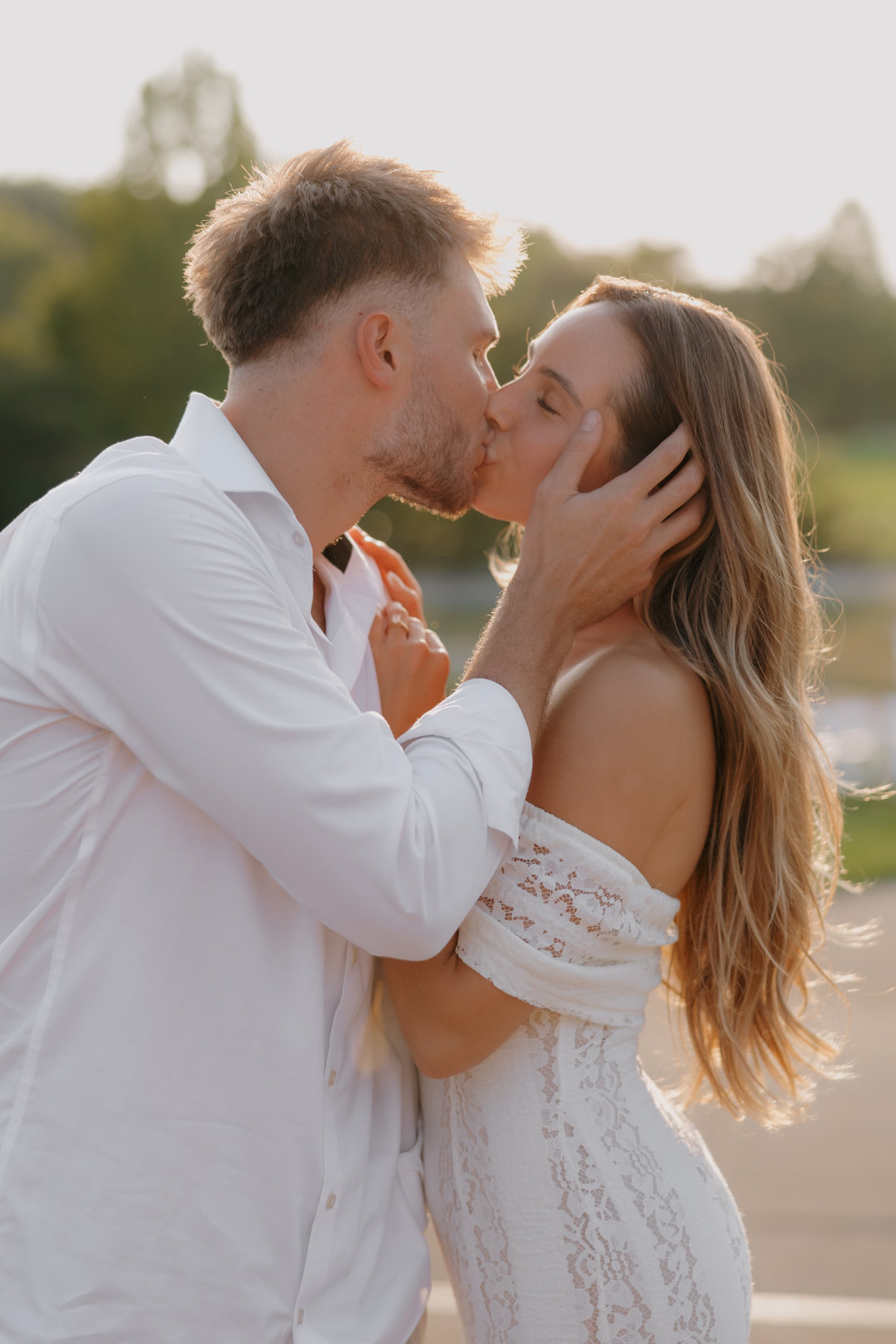 The couple sharing a kiss in warm golden light while standing outdoors.