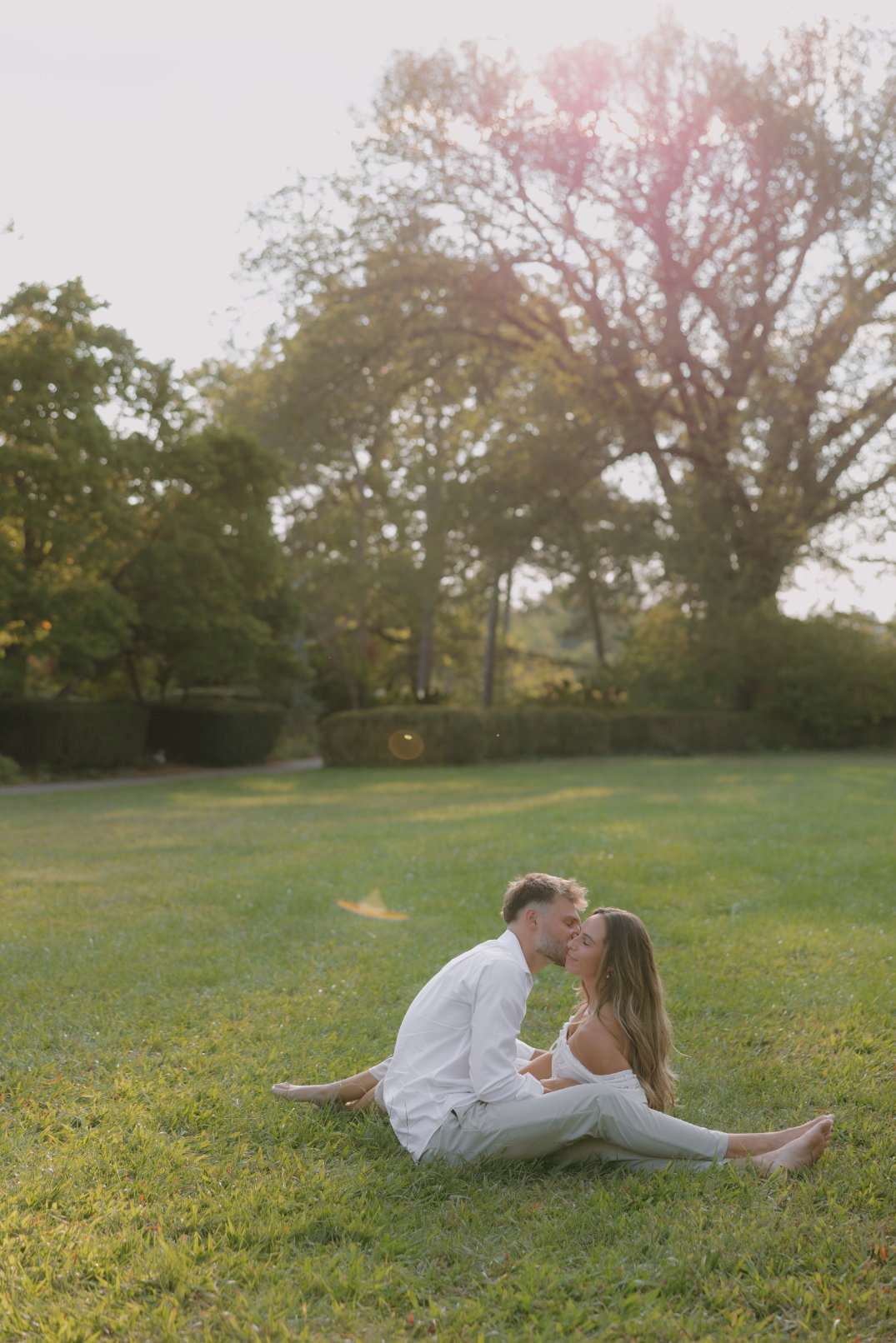 The couple sitting close together on the grass, with trees and open sky in the background in Cincinnati, Ohio.