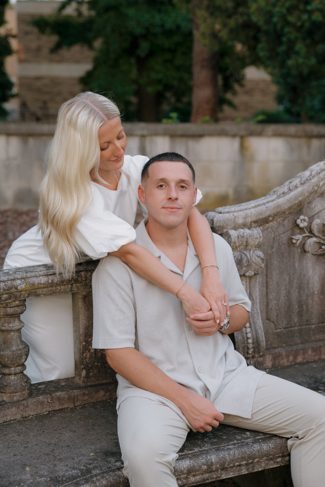 The bride standing behind her partner with her arms around his shoulders, smiling softly.