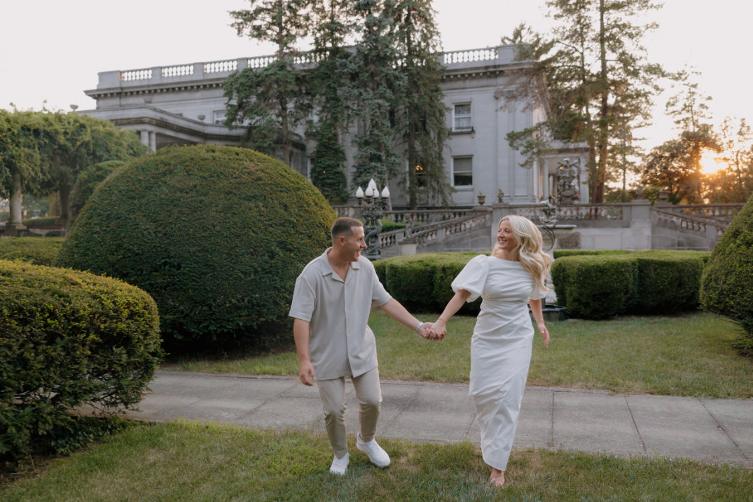 The couple walking toward the camera while holding hands, framed by gardens at Laurel Court, Cincinnati.