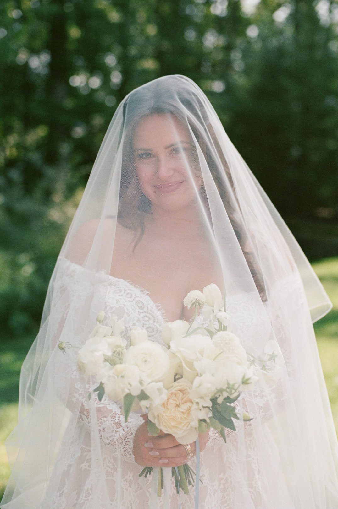 Bridal portrait with the bride holding her bouquet and smiling softly through her veil.