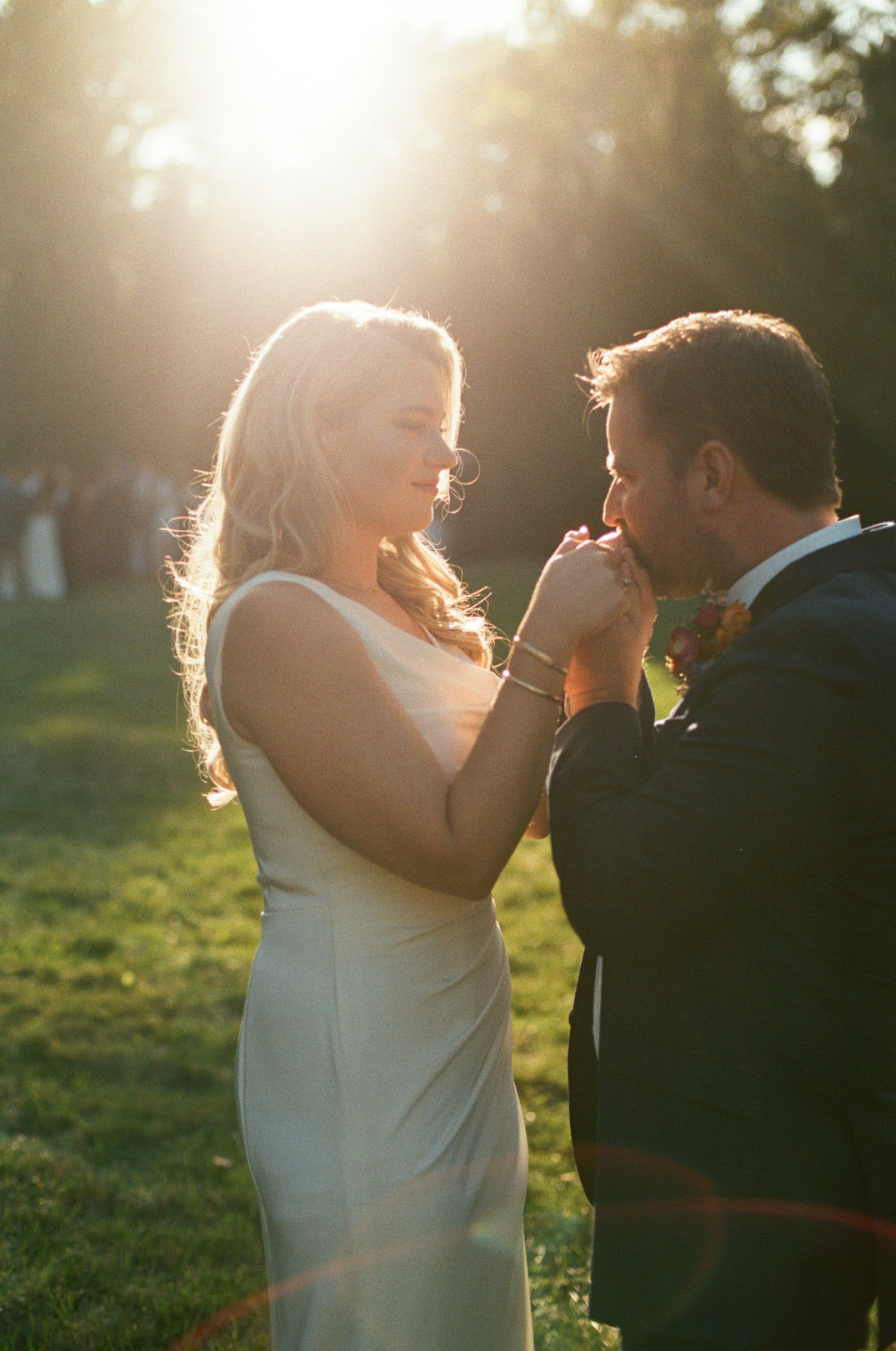 An Ohio couple stands in a sunlit field, the man gently kissing the woman's hand. She wears a white dress; he is in a dark suit. Romantic, warm atmosphere.
