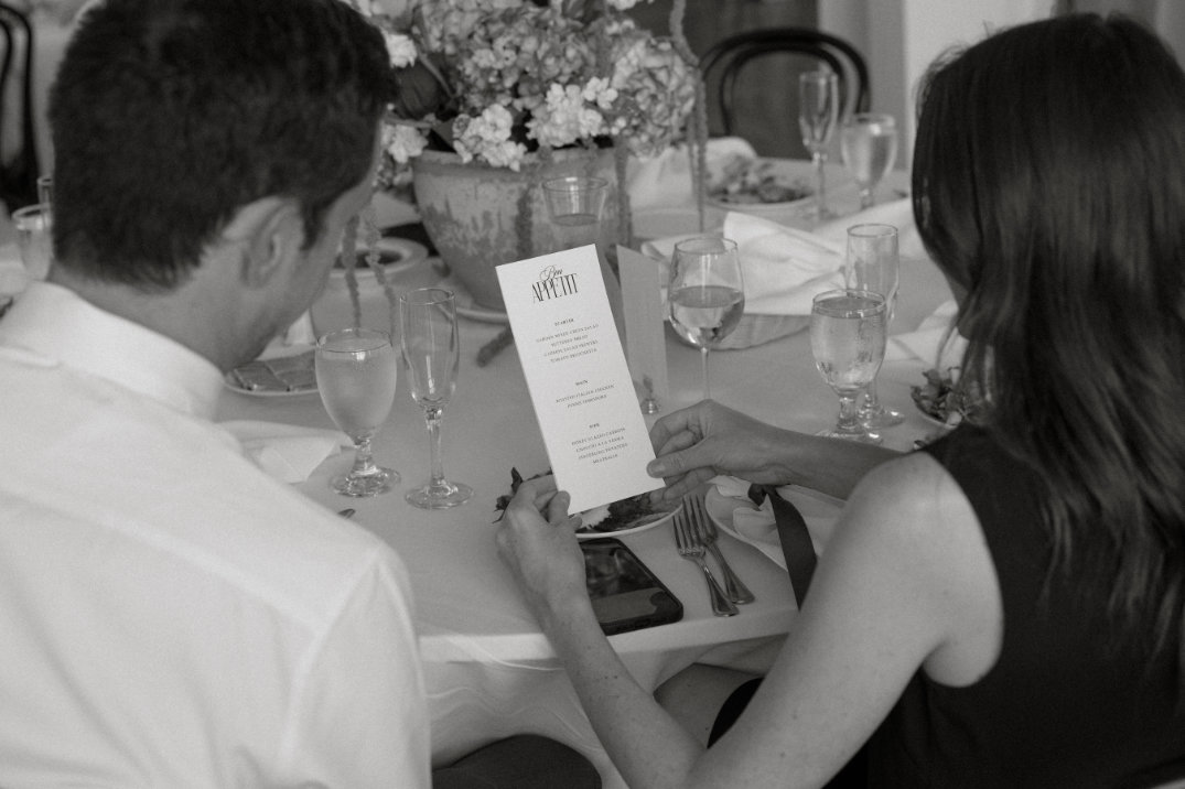 Guests seated at a reception table, reading the menu and sharing a quiet conversation.
