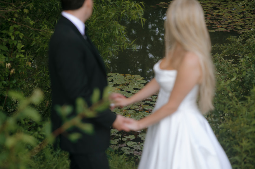 The couple holding hands and walking through greenery, captured candidly from the side.