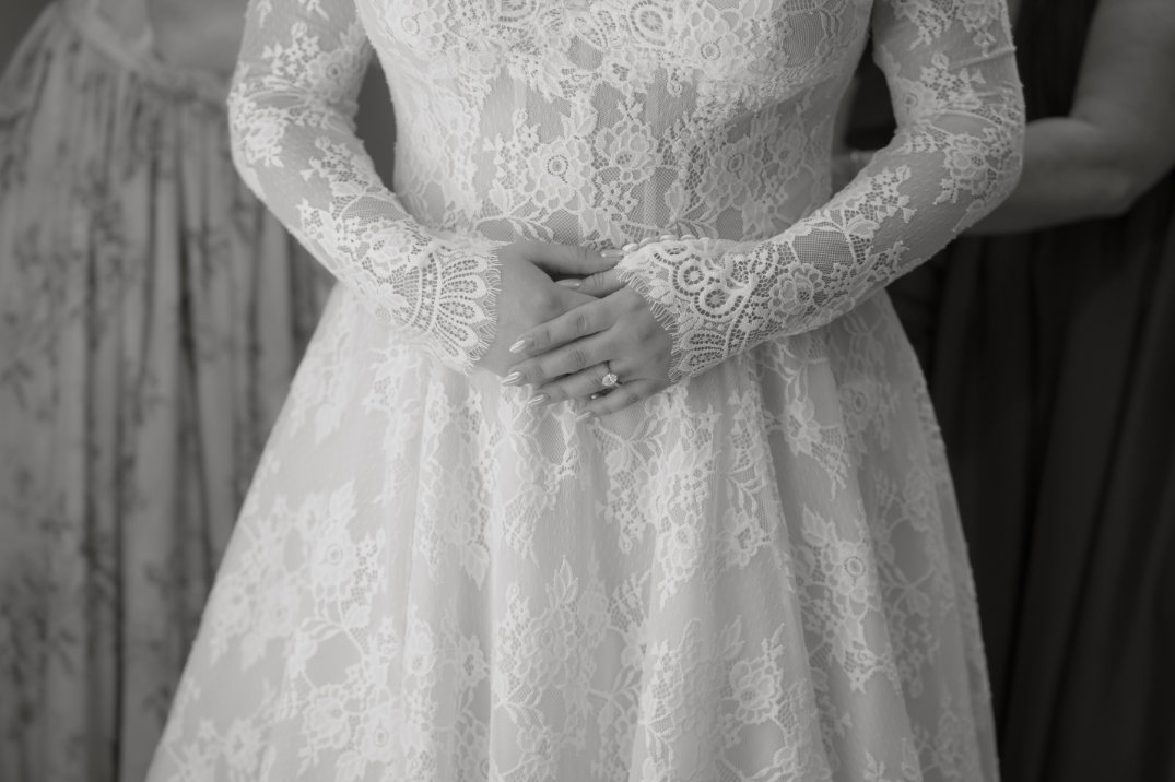 Close-up detail of the bride’s lace wedding dress with hands gently folded at the waist.