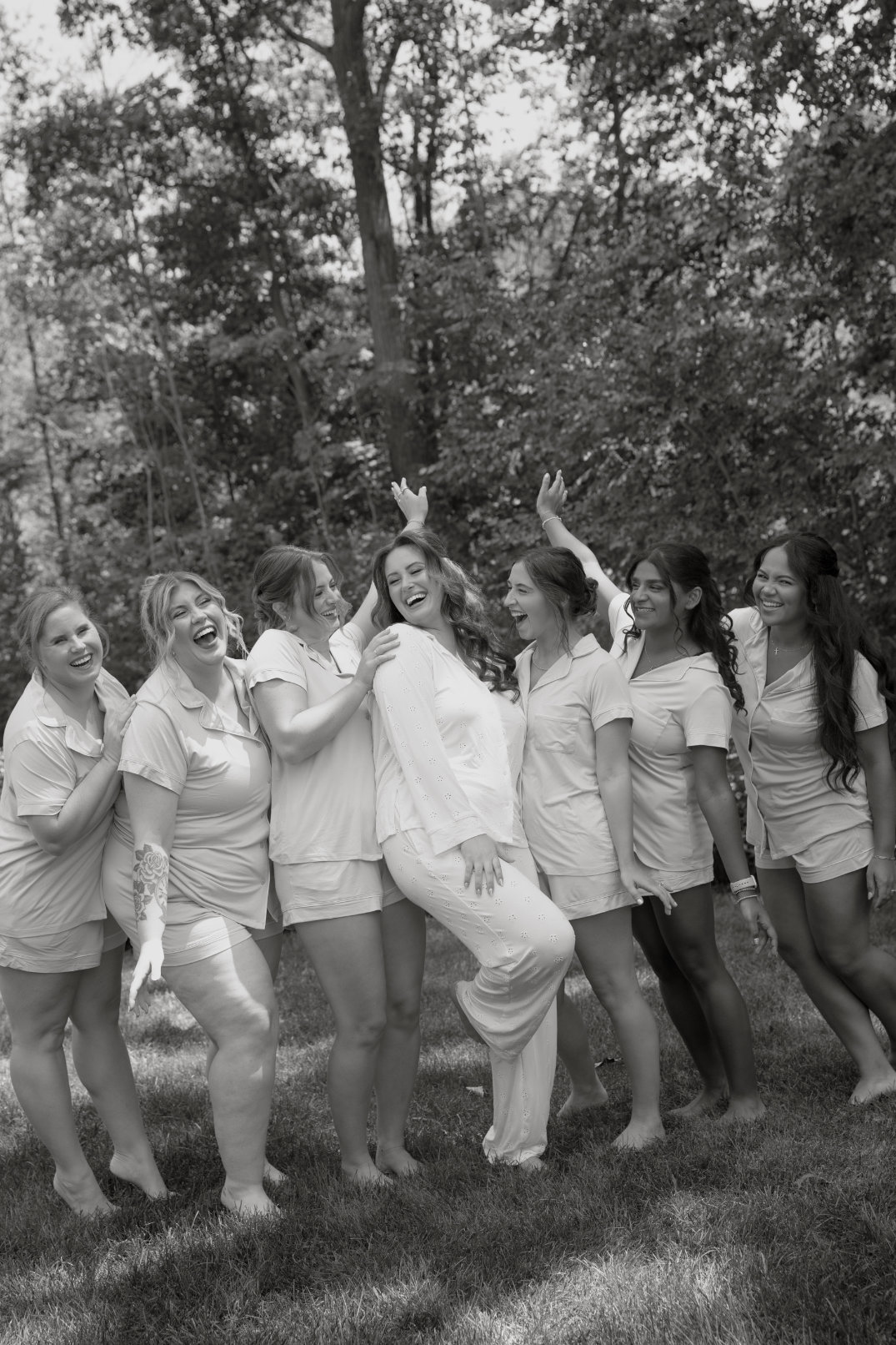 Black and white photo of bridesmaids laughing and walking arm in arm outdoors.