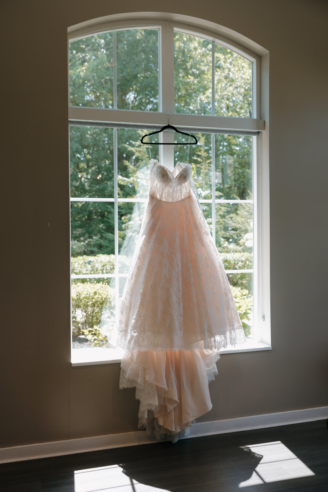 Wedding dress hanging in front of a window, softly lit and centered in the frame.
