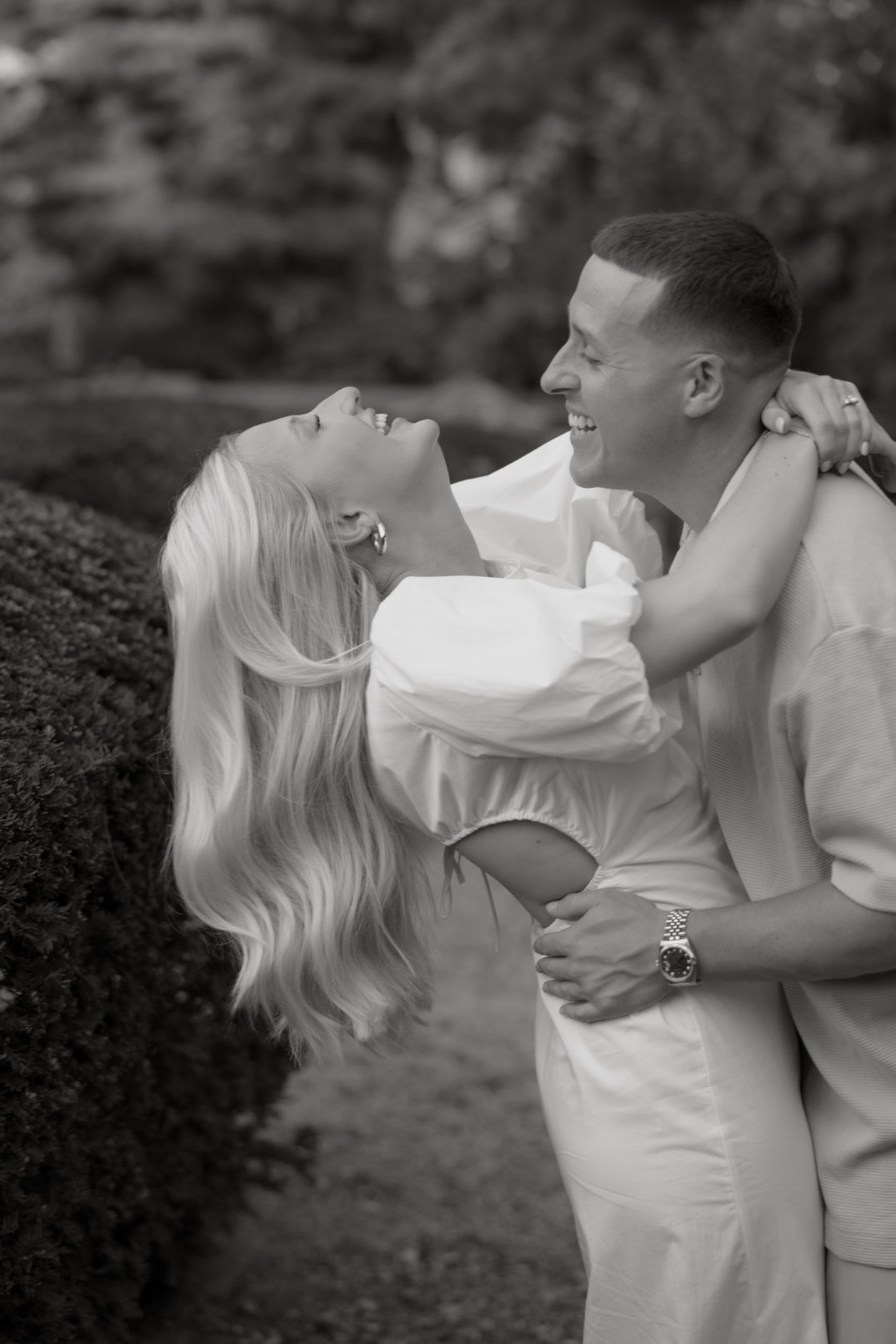 Black and white photo of the couple laughing as they hold each other closely.