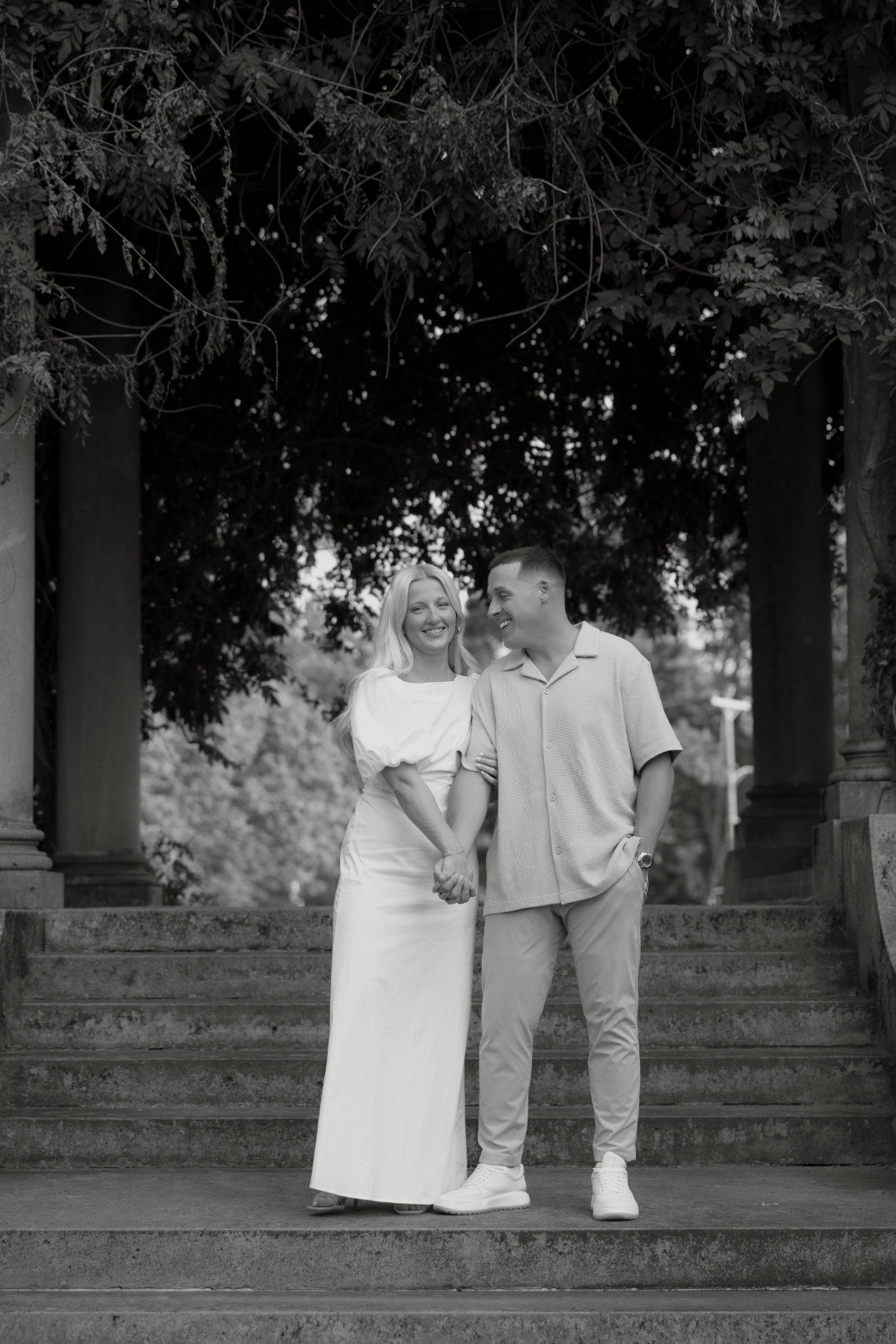 Black and white portrait of the couple walking together beneath tall trees, captured by Chloe Elizabeth Photography.