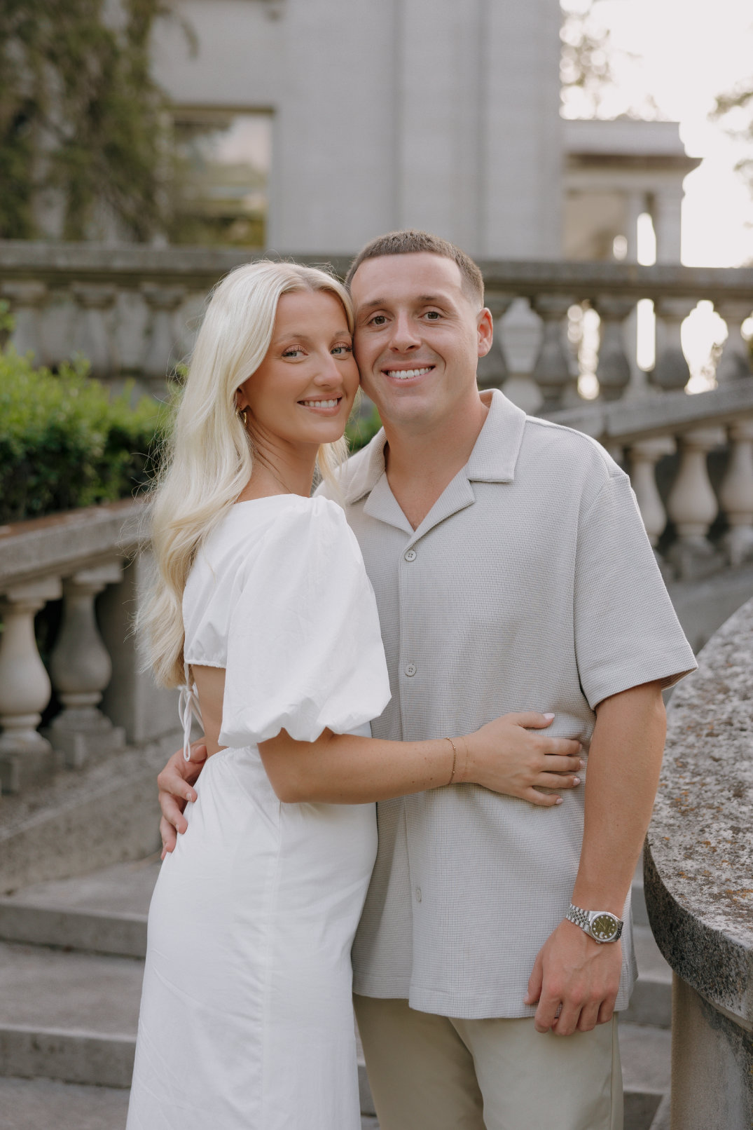 Close-up portrait of the couple smiling at the camera while standing arm in arm outdoors.