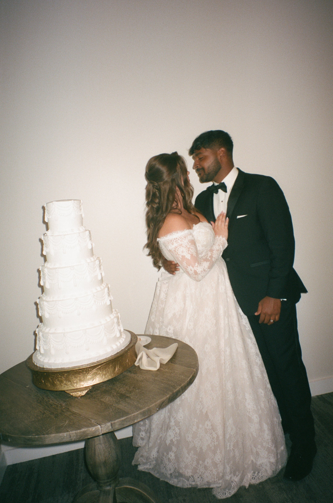 The couple standing beside their wedding cake, sharing a quiet moment together.