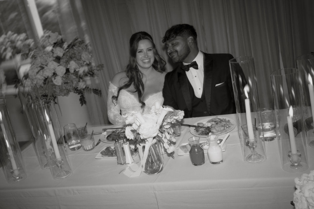 Black and white reception table scene with the couple seated and guests nearby.