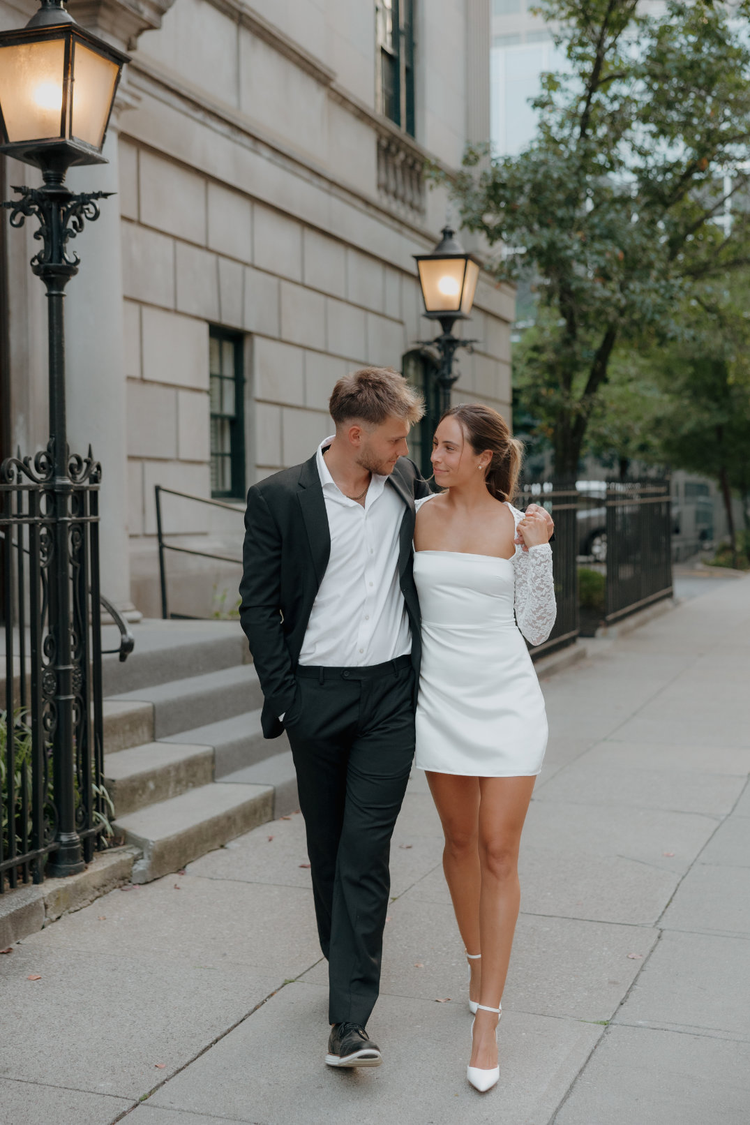 The couple walking together along a tree-lined pathway near a columned structure at Ault Park.