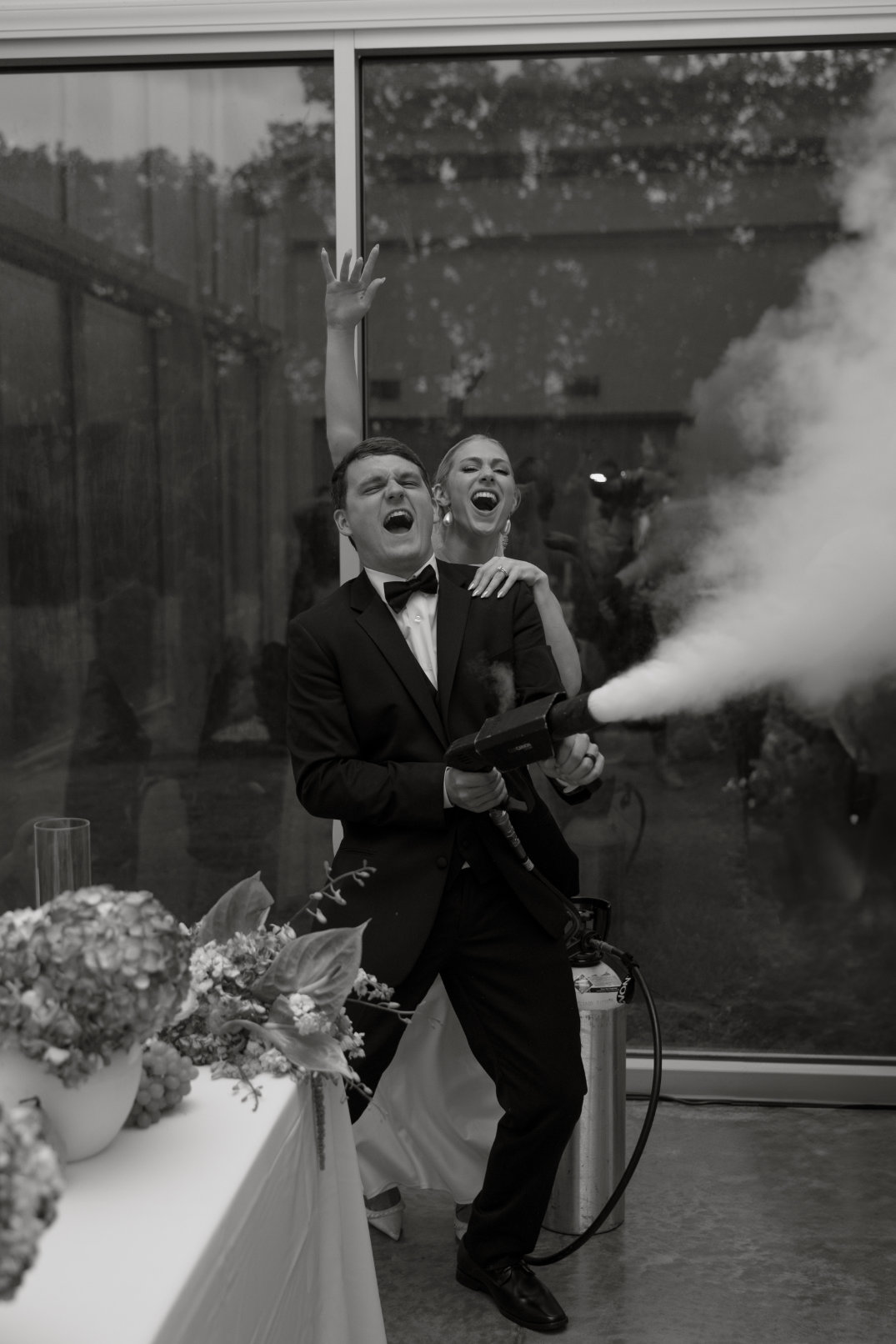 Black and white image of the groom spraying champagne in celebration, surrounded by guests.