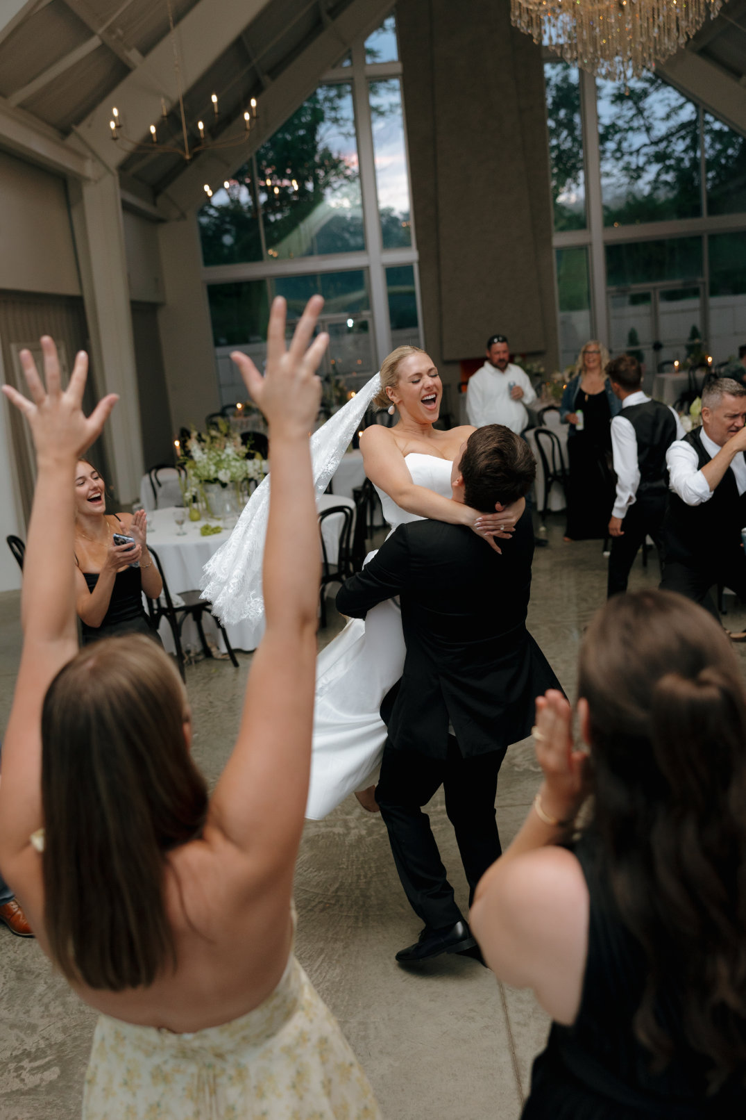 Lively dance floor moment with guests cheering and raising their hands during the reception.