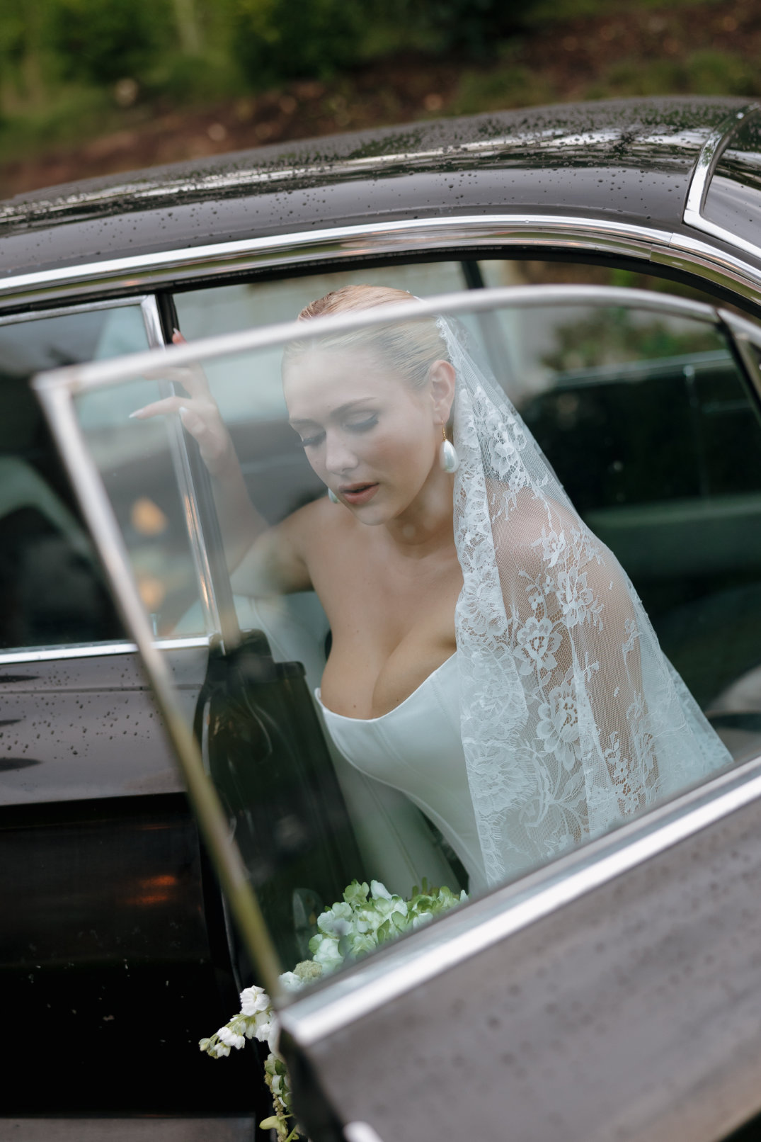 Close-up portrait of the bride sitting inside a vintage car, framed through the window.