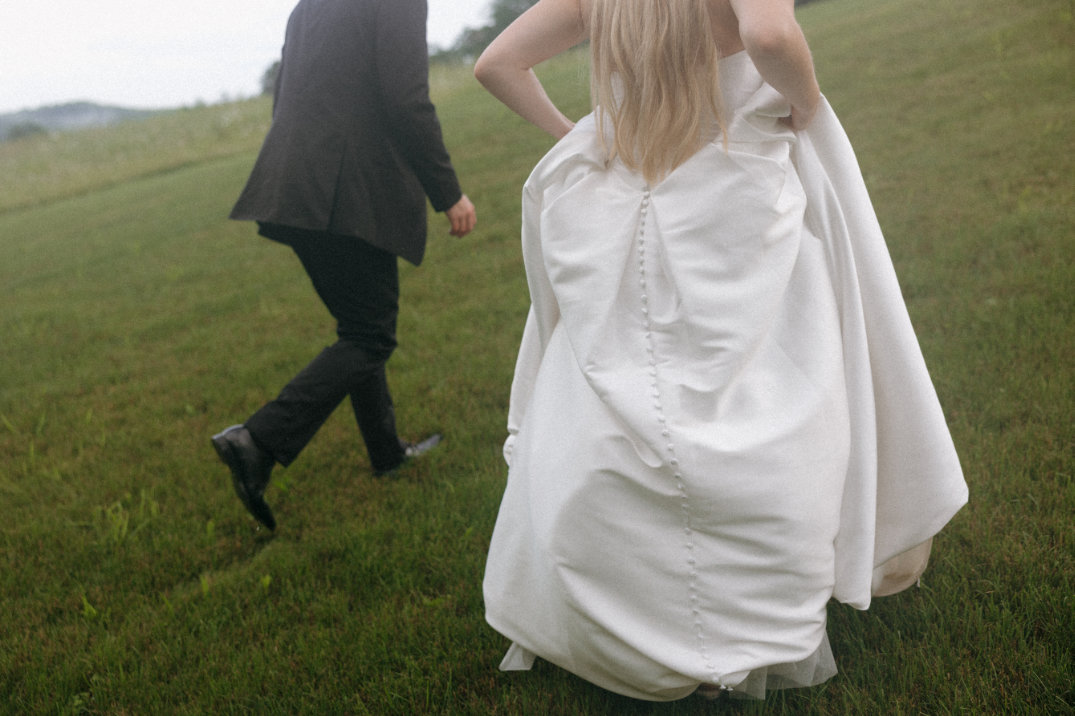 Candid photo of the bride lifting her dress while walking across the lawn at The Seventy Five Venue in Hocking Hills, Ohio, captured by Chloe Elizabeth Photography.
