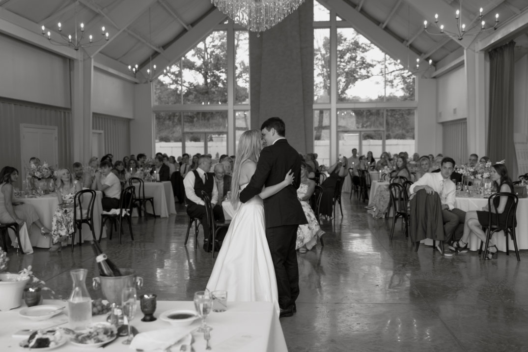 Black and white photograph of the couple sharing their first dance indoors.