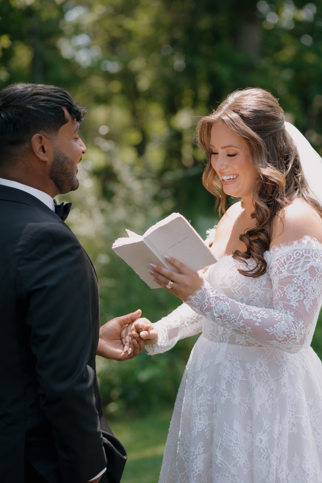 Bride reading vows from a booklet, smiling as she looks at her partner.